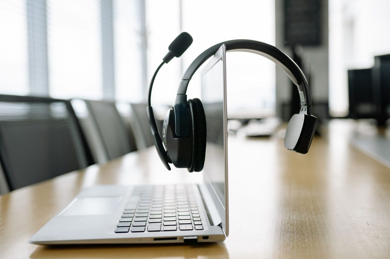 Auriculares con micrófono sobre un ordenador portátil abierto, en una mesa de reuniones de madera