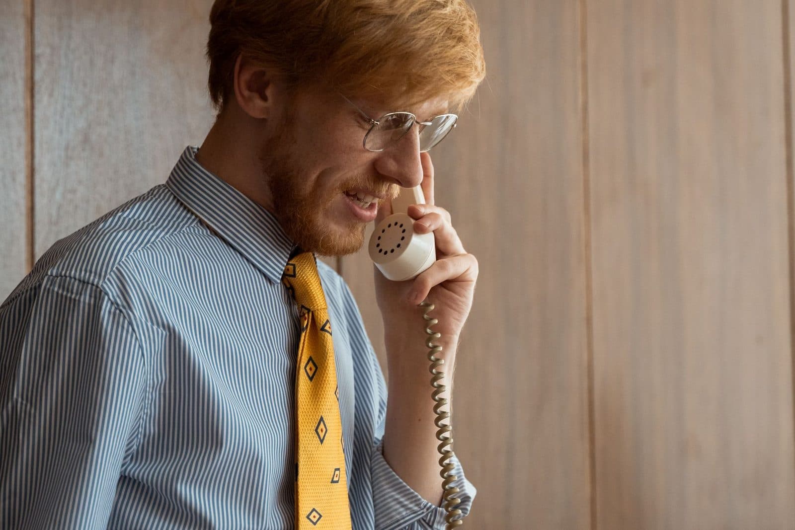 Homme à lunettes en chemise rayée et cravate jaune téléphonant avec un combiné filaire beige