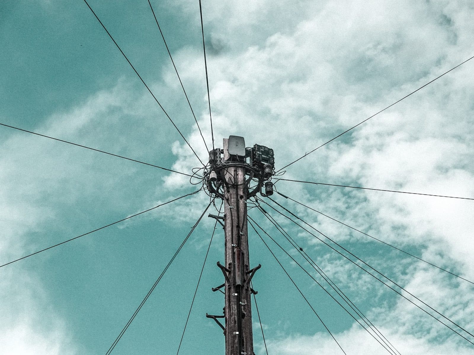 Poteau téléphonique en bois avec boîtiers de raccordement et nombreux câbles aériens sous un ciel nuageux