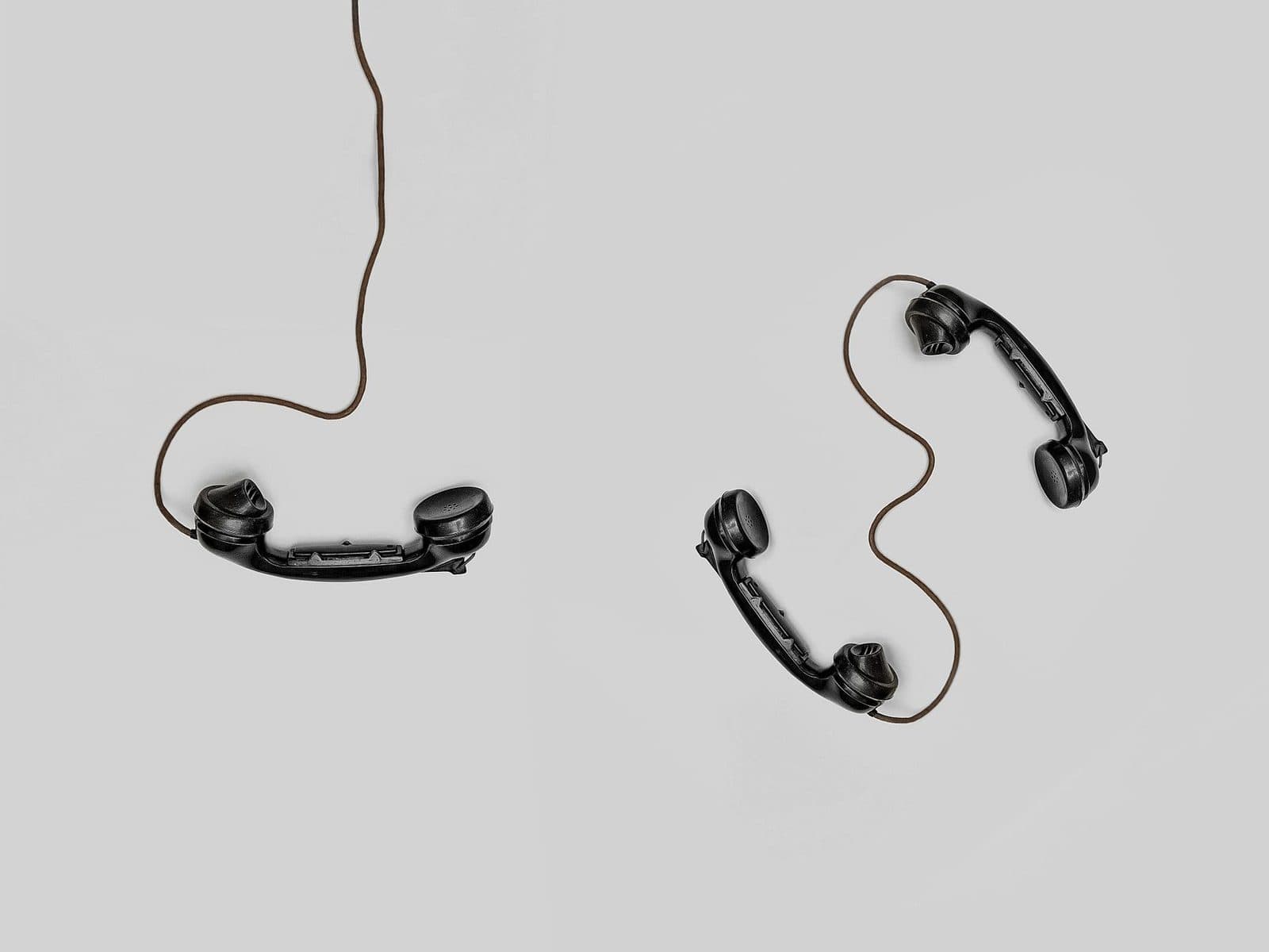 Deux combinés de téléphones fixes noirs avec leurs cordons, posés sur un fond gris clair