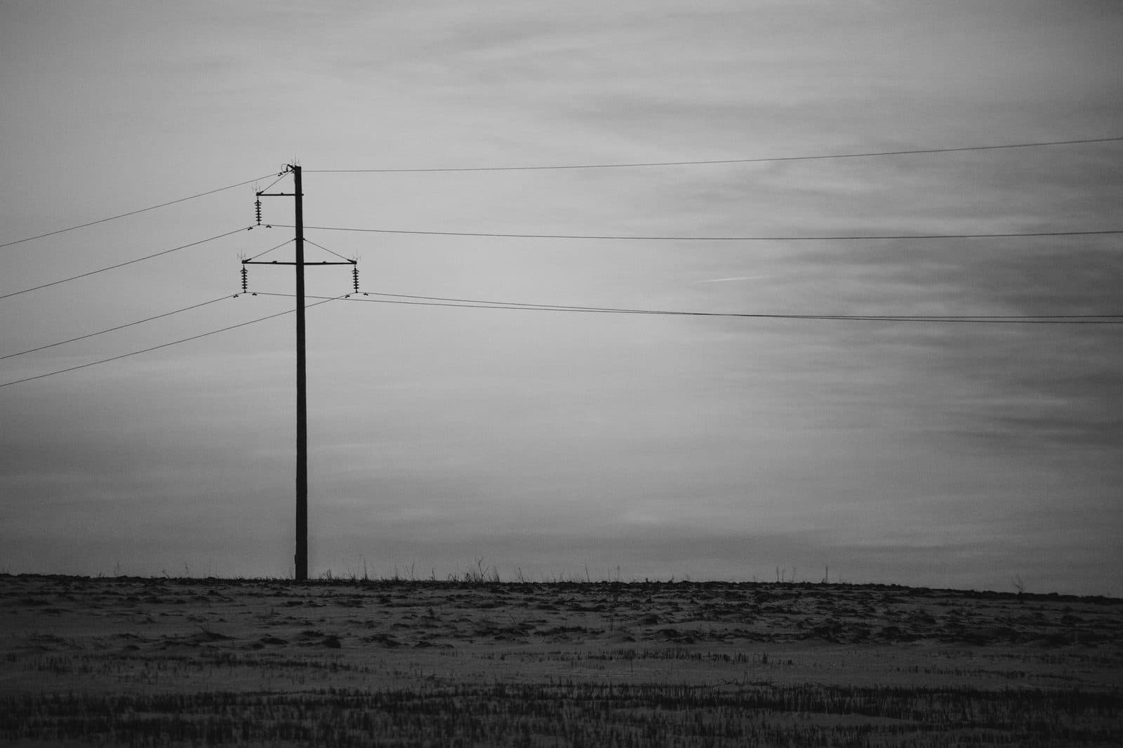 Palo telegrafico isolato con linee aeree in un campo, cielo grigio, fotografia in bianco e nero
