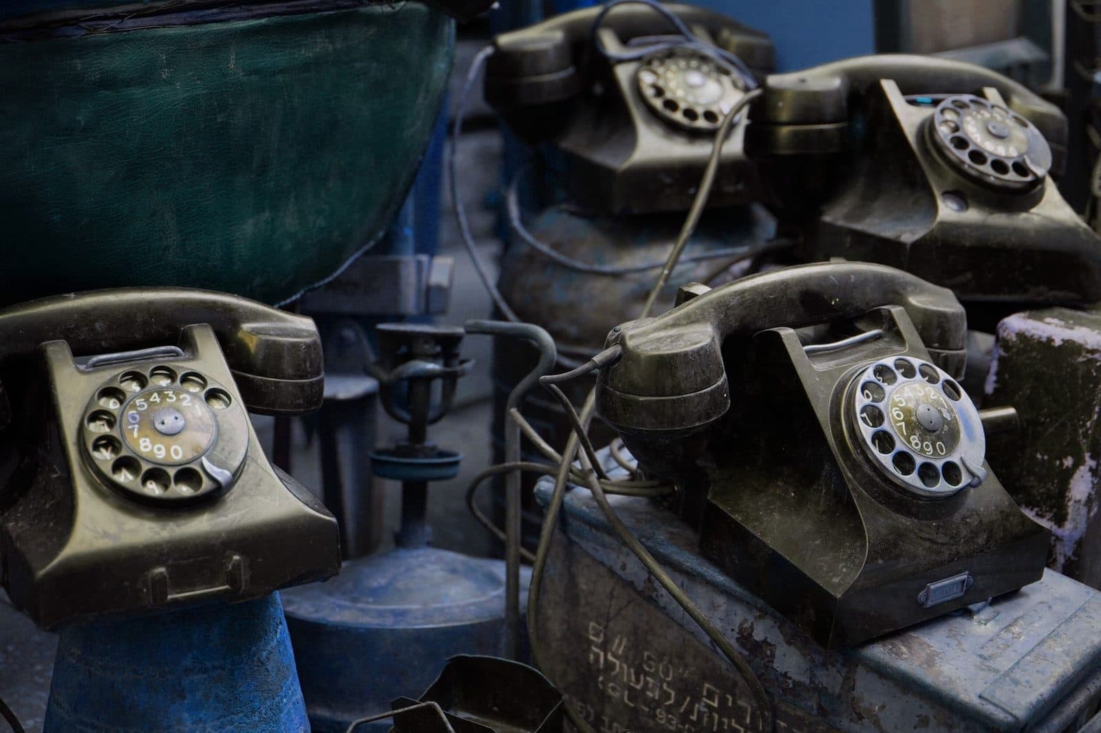 Old black bakelite rotary landline telephones piled up with their cables on metal crates