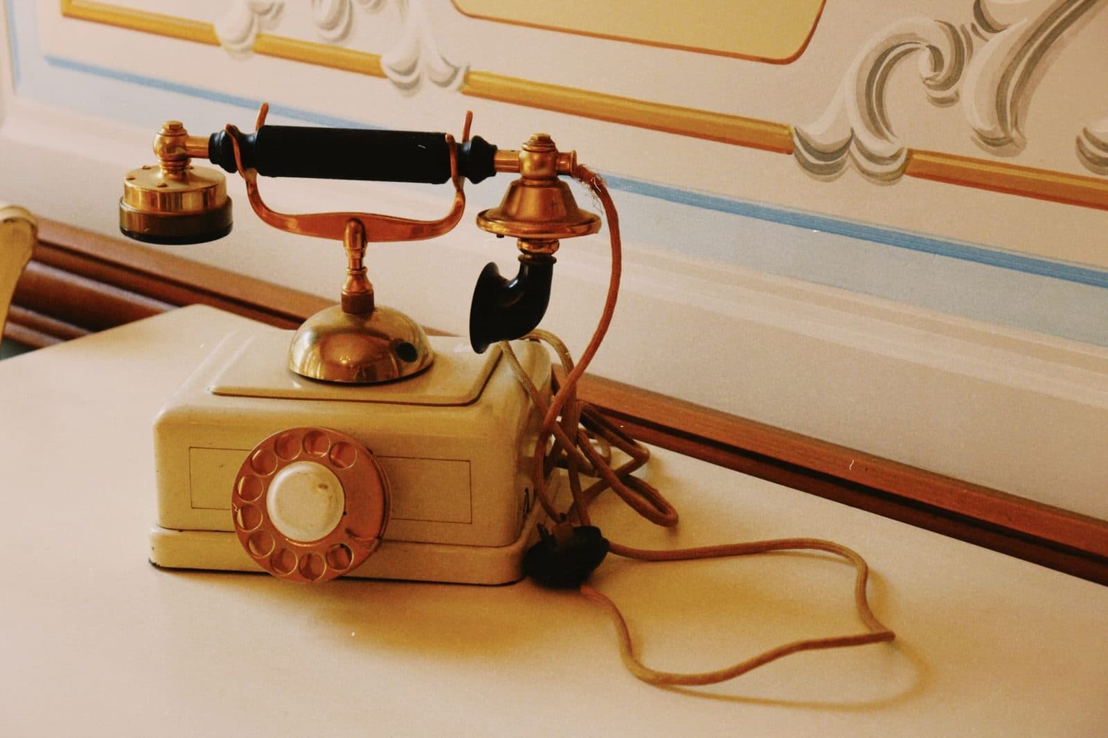 Antique brass and ivory rotary dial telephone sitting on a table with its cord