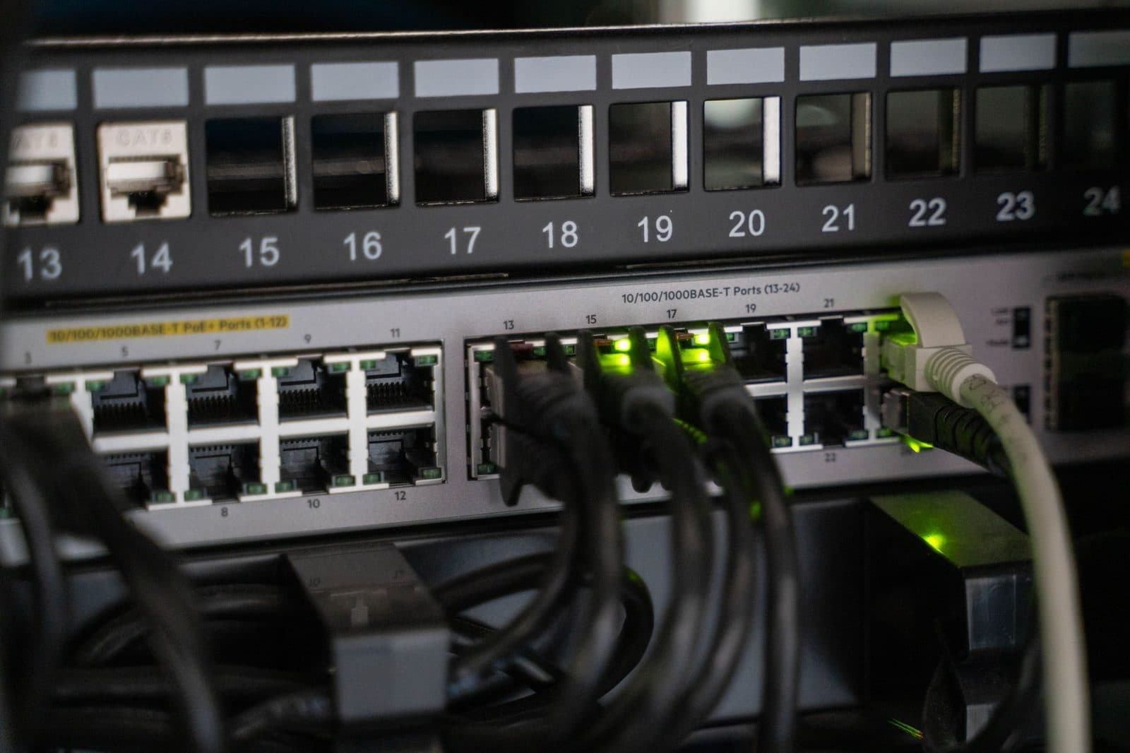 Close-up of a network switch and patch panel with Ethernet cables plugged in and green indicator lights