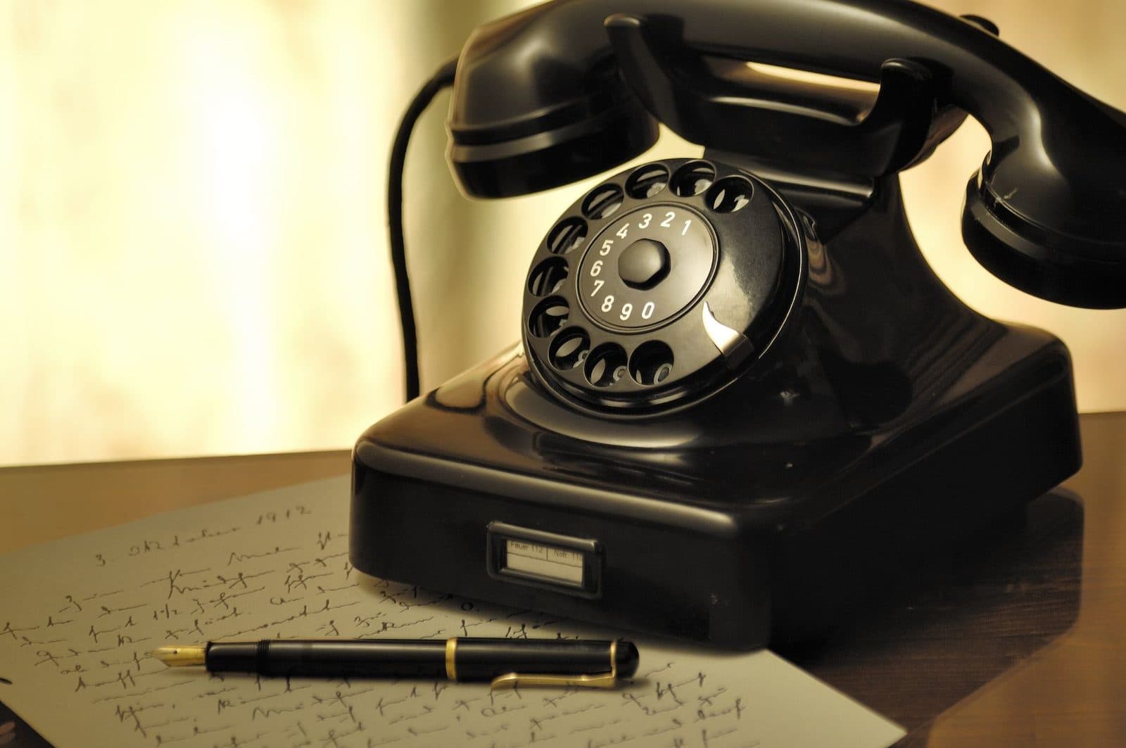 Telefono nero vintage a disco appoggiato su una scrivania, accanto a una penna stilografica e a una lettera manoscritta