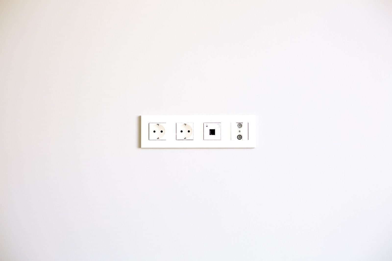 White wall plate with two power sockets, an RJ45 socket and TV sockets on a light-coloured wall