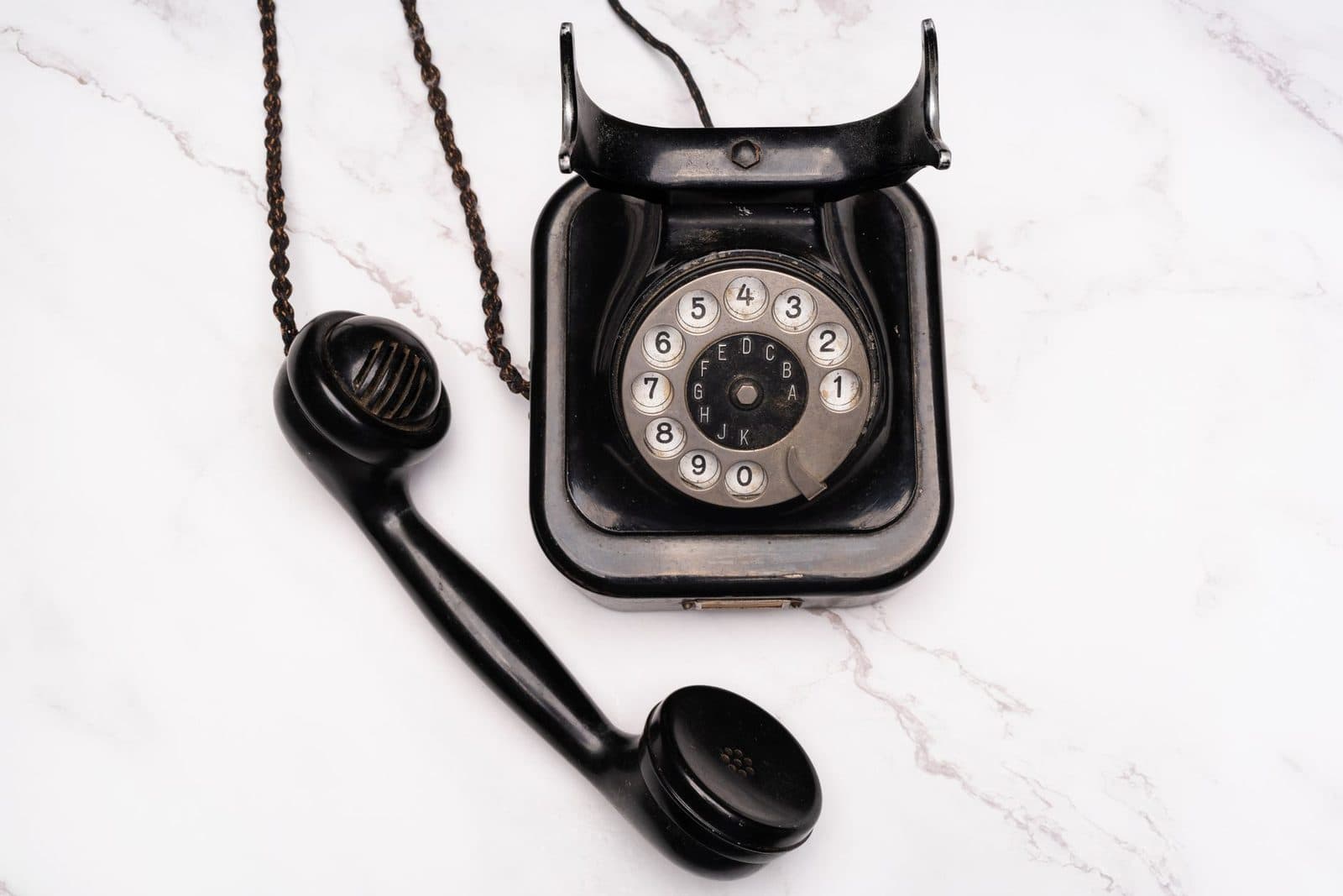 Altes schwarzes Wählscheibentelefon, abgenommener Hörer auf weißem Marmoruntergrund