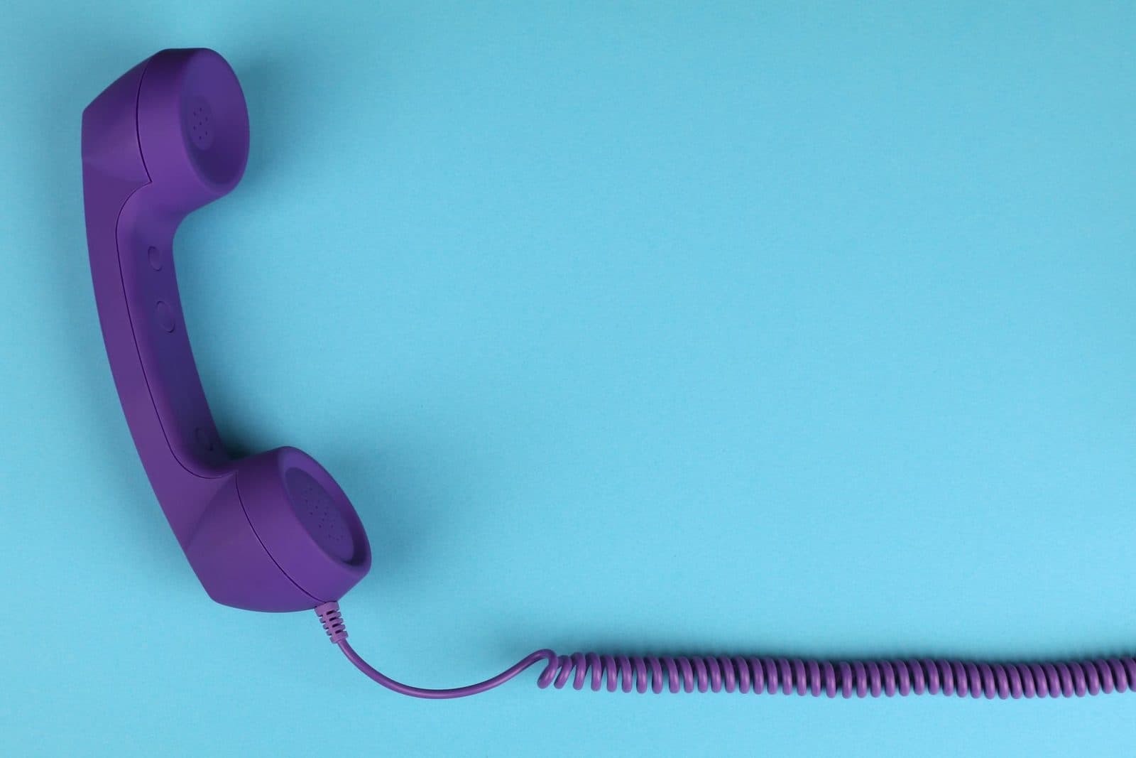 Violetter Festnetz-Telefonhörer mit Spiralkabel auf blauem Hintergrund
