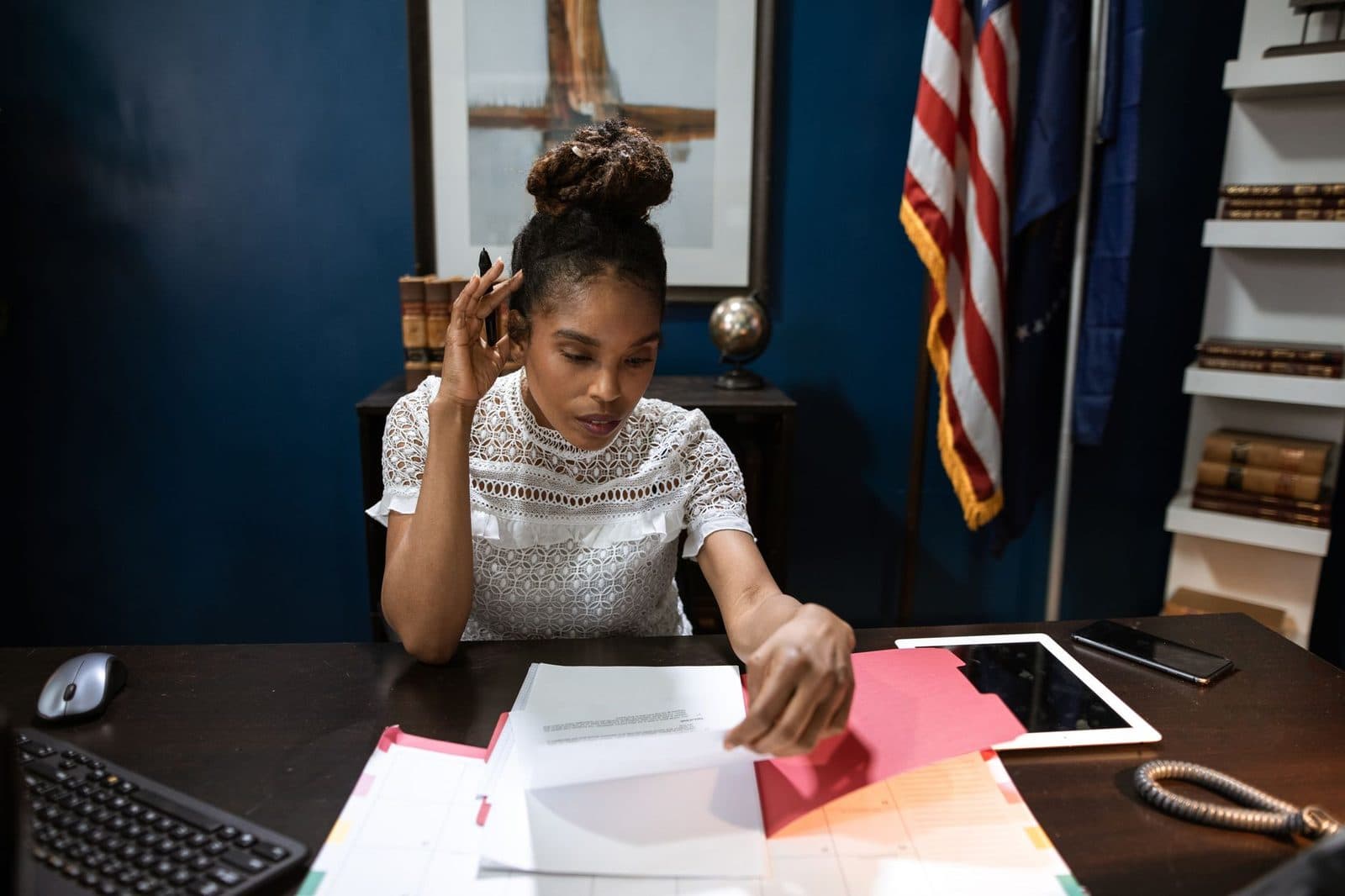 Femme au téléphone triant des documents dans un bureau administratif avec drapeau américain et tablette