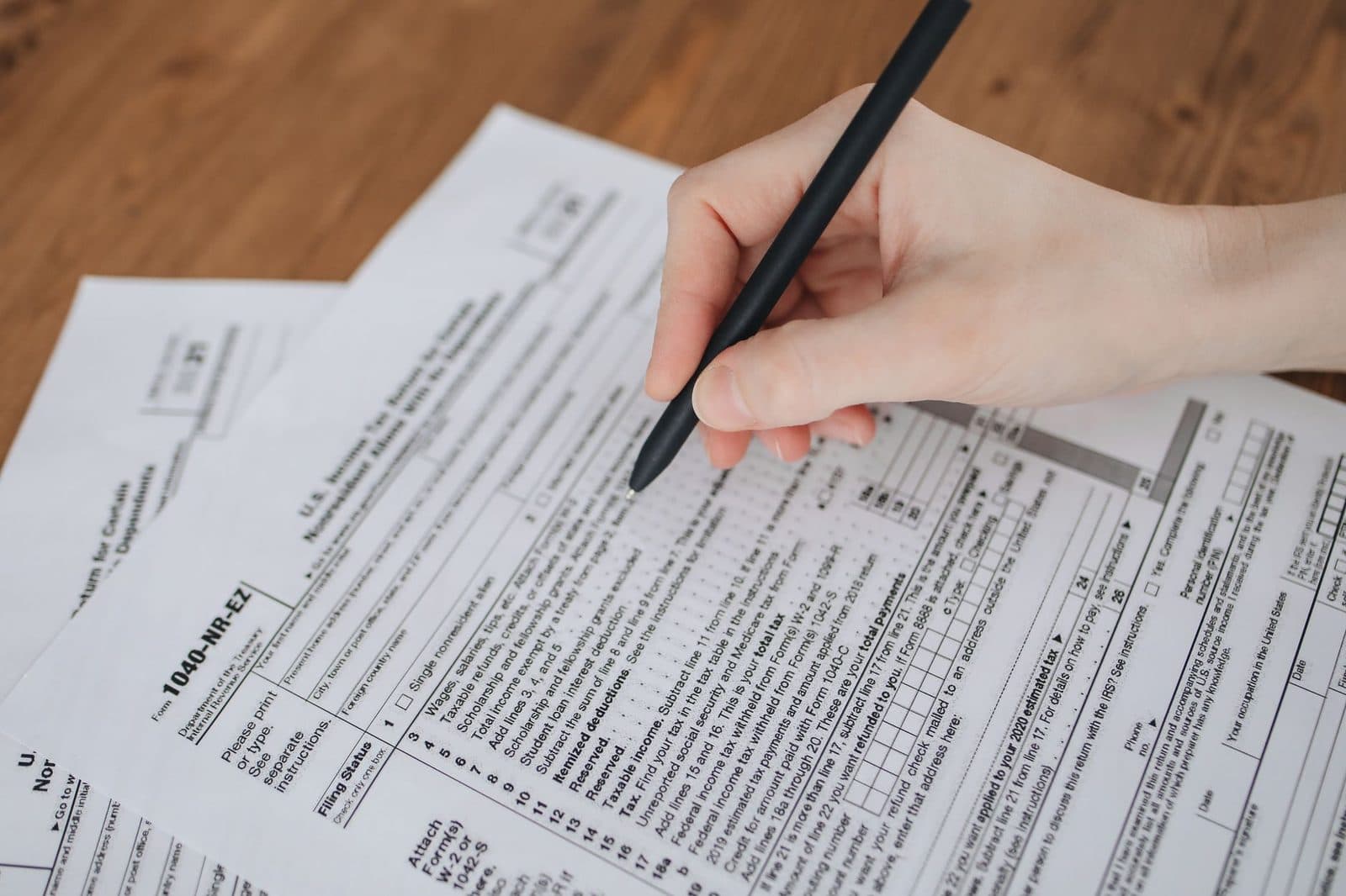 Main tenant un stylo au-dessus de formulaires administratifs fiscaux posés sur une table en bois