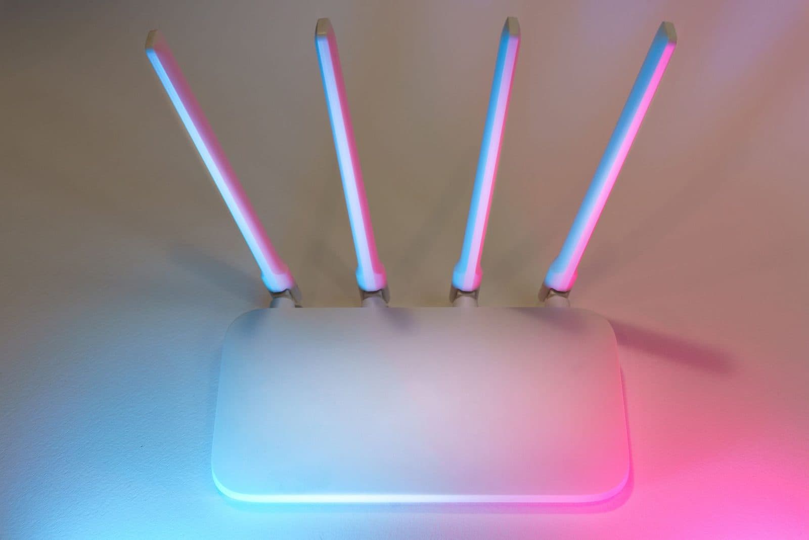 Router Wi-Fi branco com quatro antenas erguidas, iluminado por luzes azuis e rosas