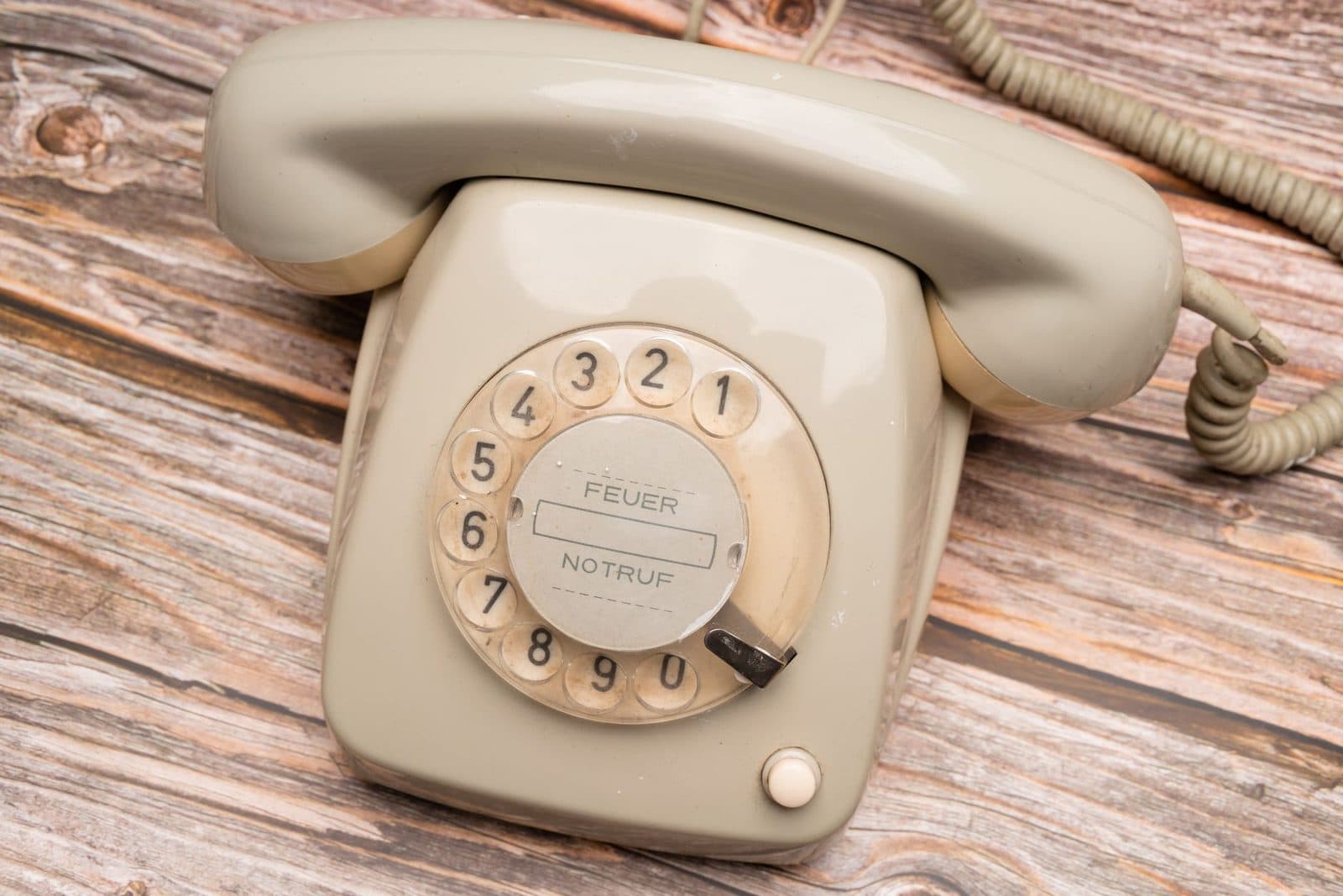 Antiguo teléfono beige de disco giratorio sobre una mesa de madera desgastada