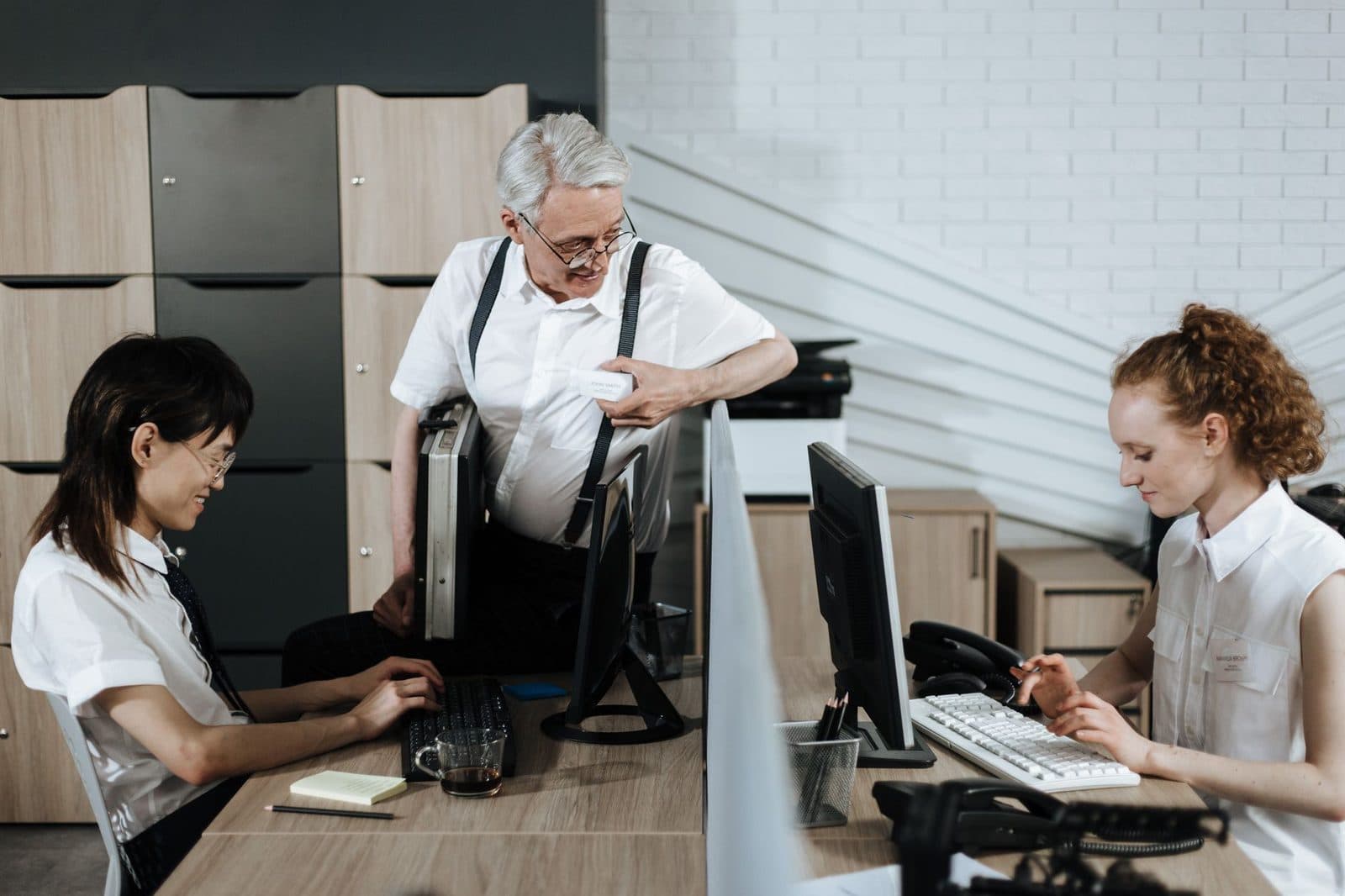 Tres colegas en una oficina con ordenadores, teléfonos fijos y una impresora multifunción al fondo
