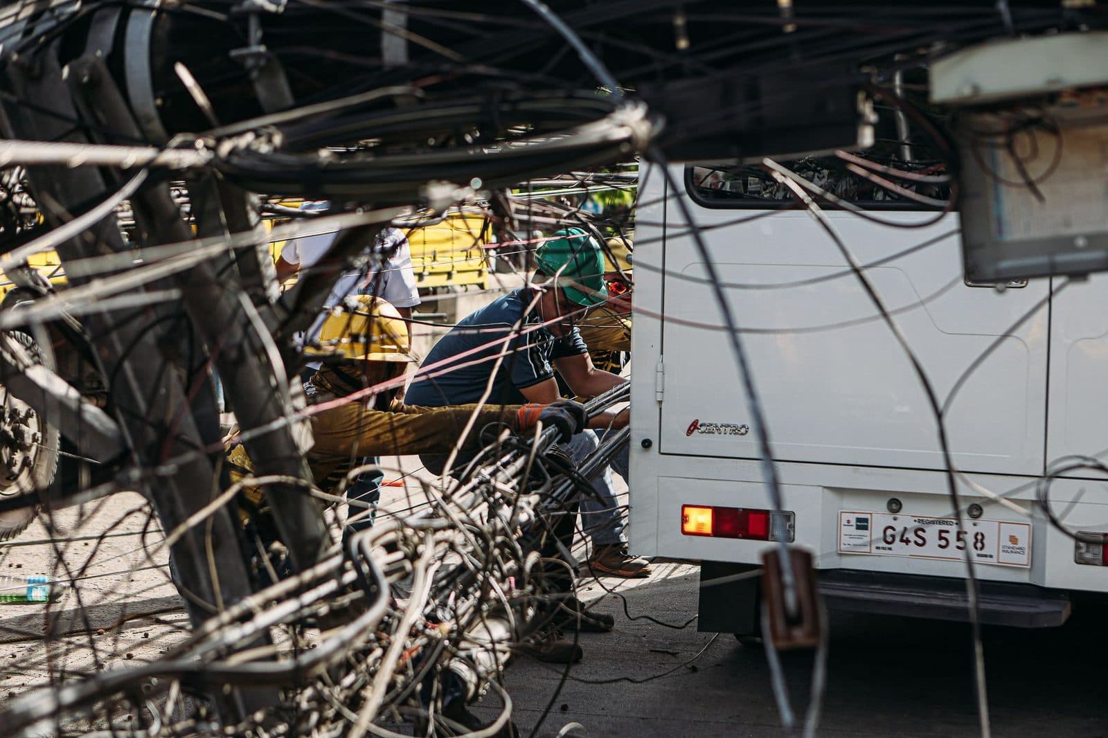 Técnicos trabajando en una maraña de cables telefónicos aéreos, junto a un autobús blanco