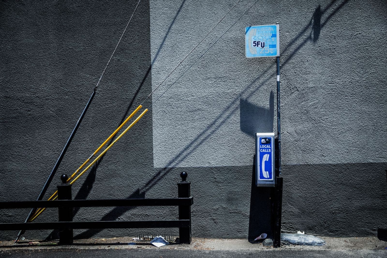 Vecchio telefono pubblico blu con la scritta «Local Calls» fissato a un muro grigio, accanto a una ringhiera nera