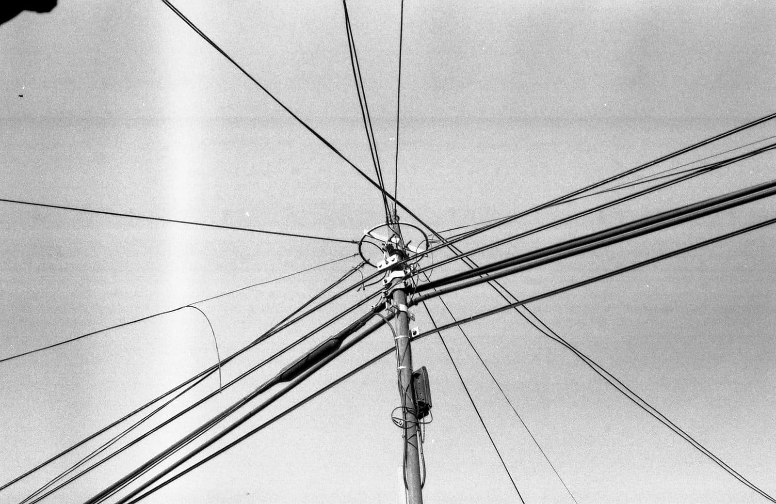 Photo en noir et blanc d'un poteau télécom avec de nombreux câbles aériens convergeant vers son sommet