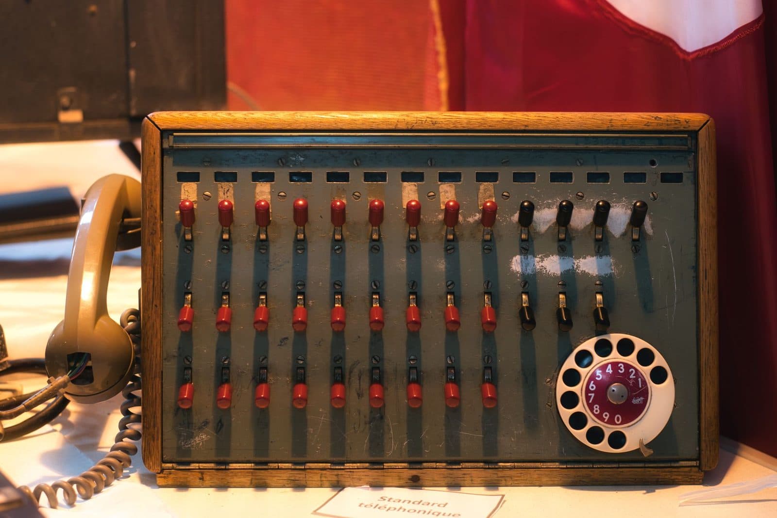 Ancien standard téléphonique en bois avec interrupteurs rouges, cadran rotatif et combiné filaire beige