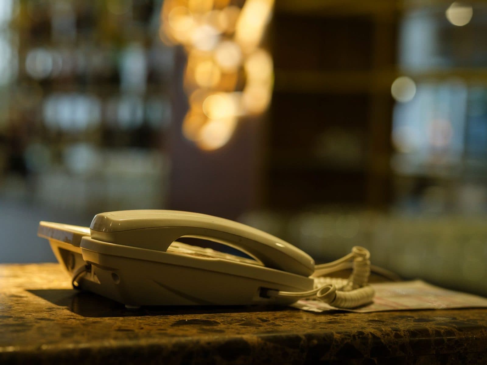 Téléphone fixe filaire blanc posé sur un comptoir en marbre, arrière-plan flou aux lumières dorées
