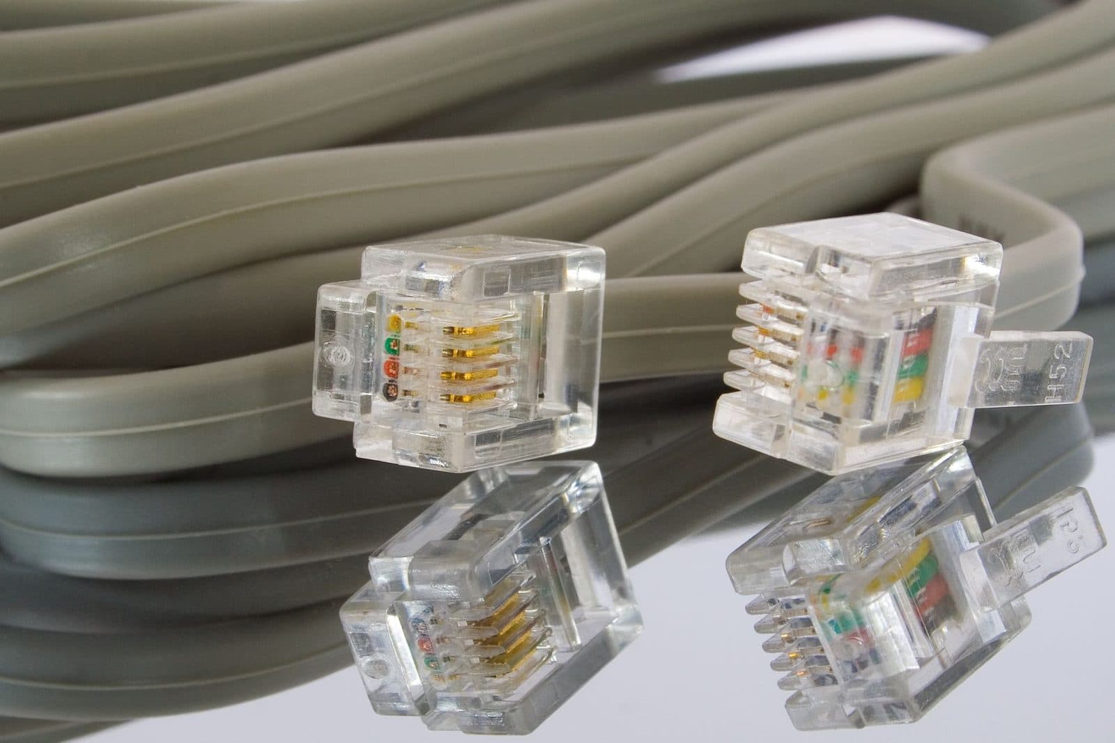 Deux connecteurs téléphoniques RJ11 transparents posés devant un câble gris enroulé