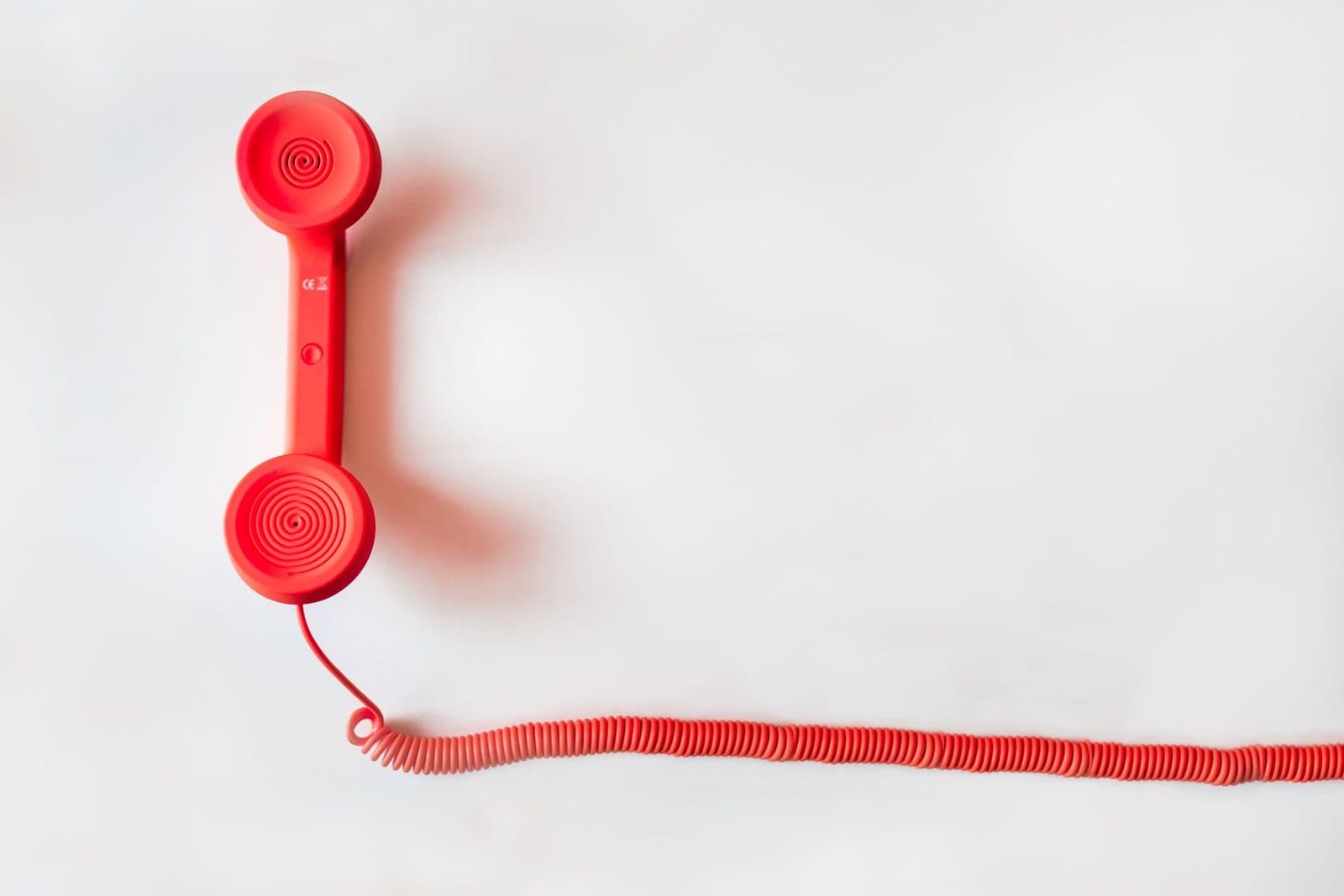 Red landline telephone handset with its coiled cord on a white background