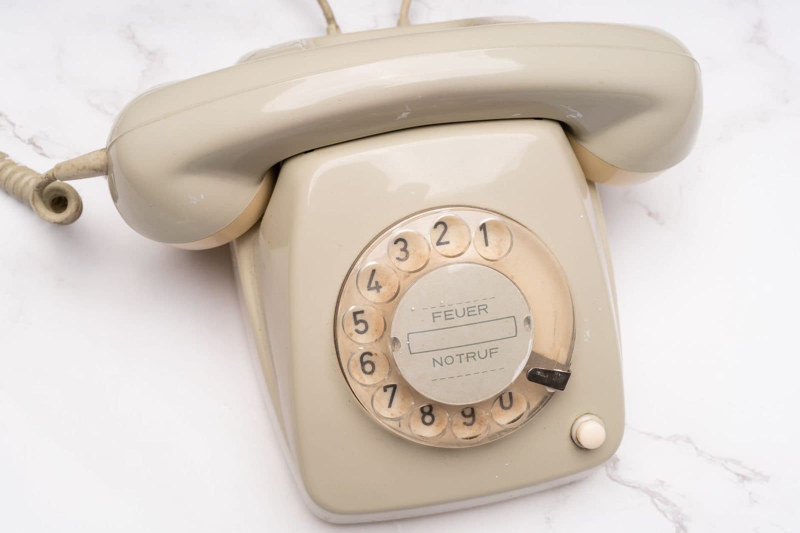 Altes beigefarbenes Festnetztelefon mit Wählscheibe, abgenommener Hörer auf einer weißen Marmorplatte
