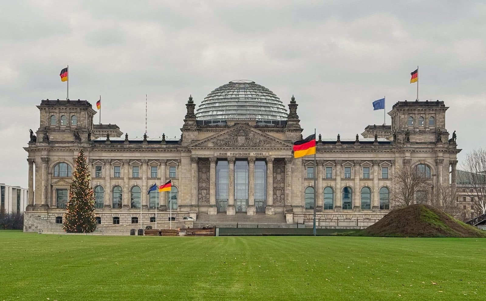 Facade of the Reichstag in Berlin with its glass dome, German flags and green lawn
