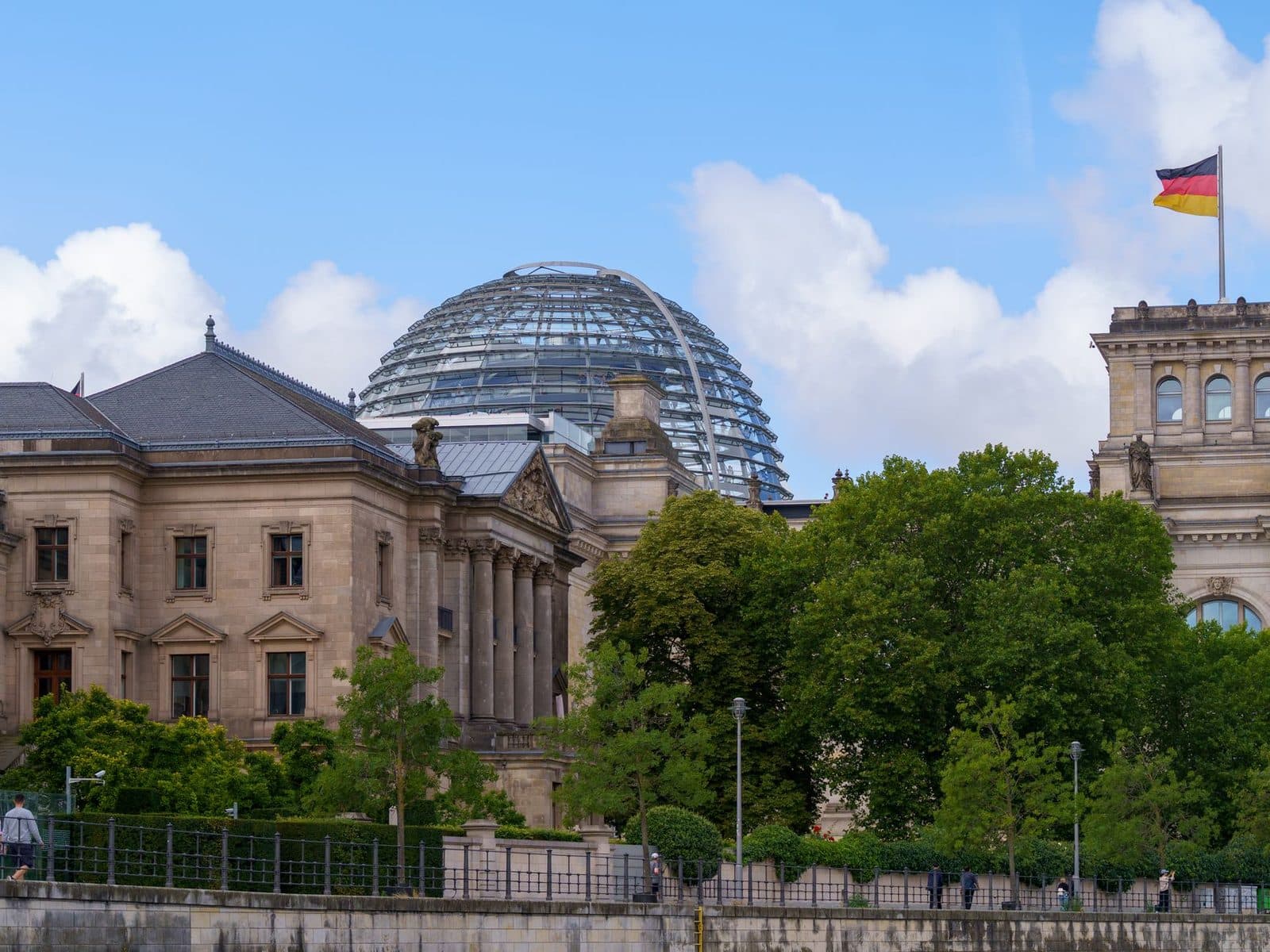 The Reichstag in Berlin with its glass dome and the German flag, surrounded by trees