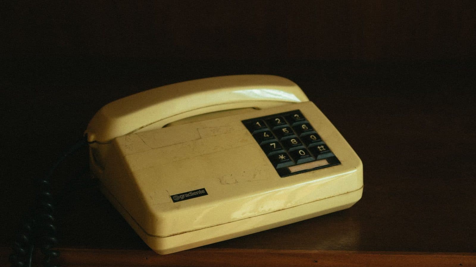 Old beige push-button landline telephone sitting on a wooden cabinet in dim light
