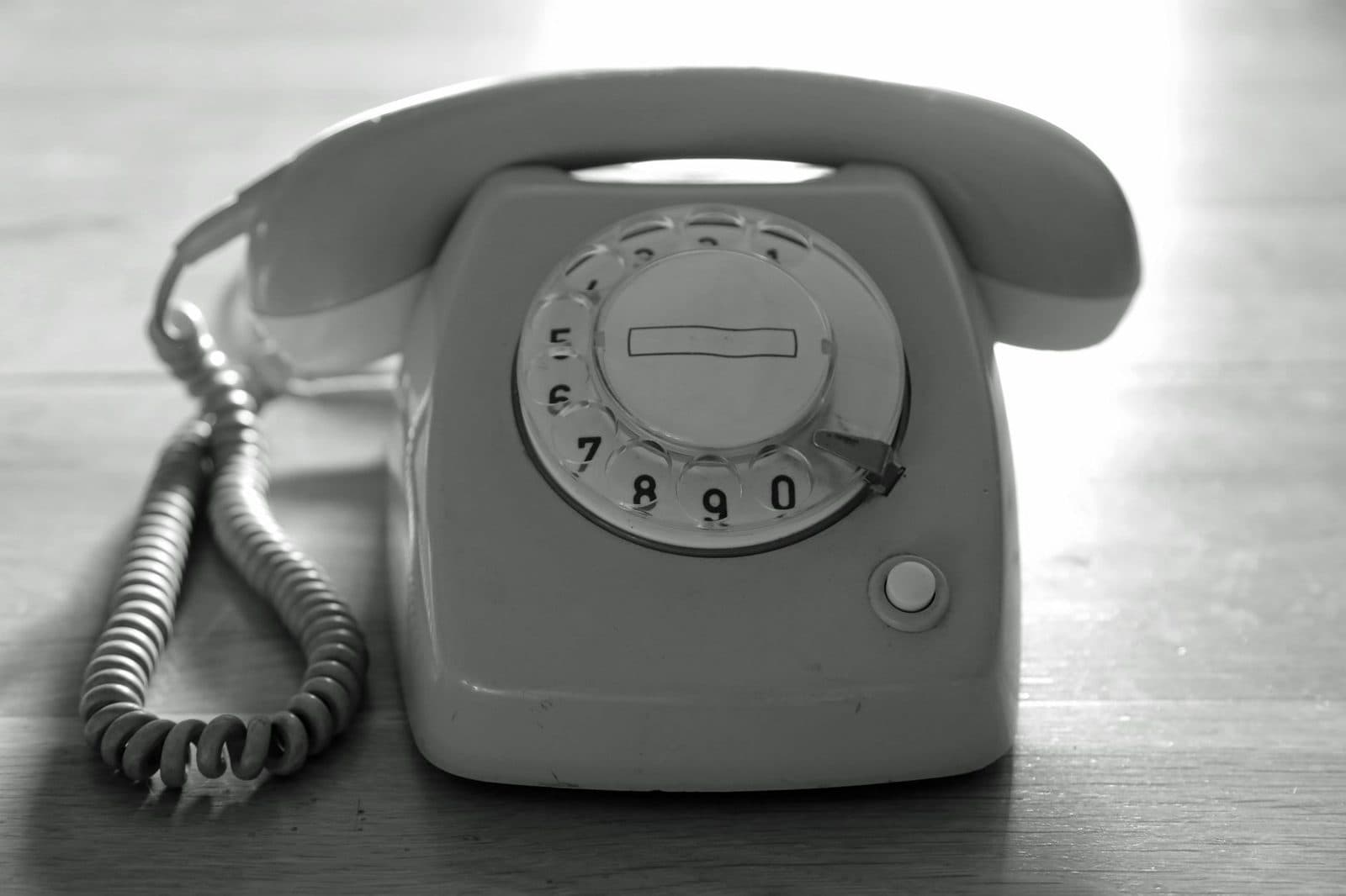 Old rotary dial landline telephone with handset and coiled cord, sitting on a wooden table