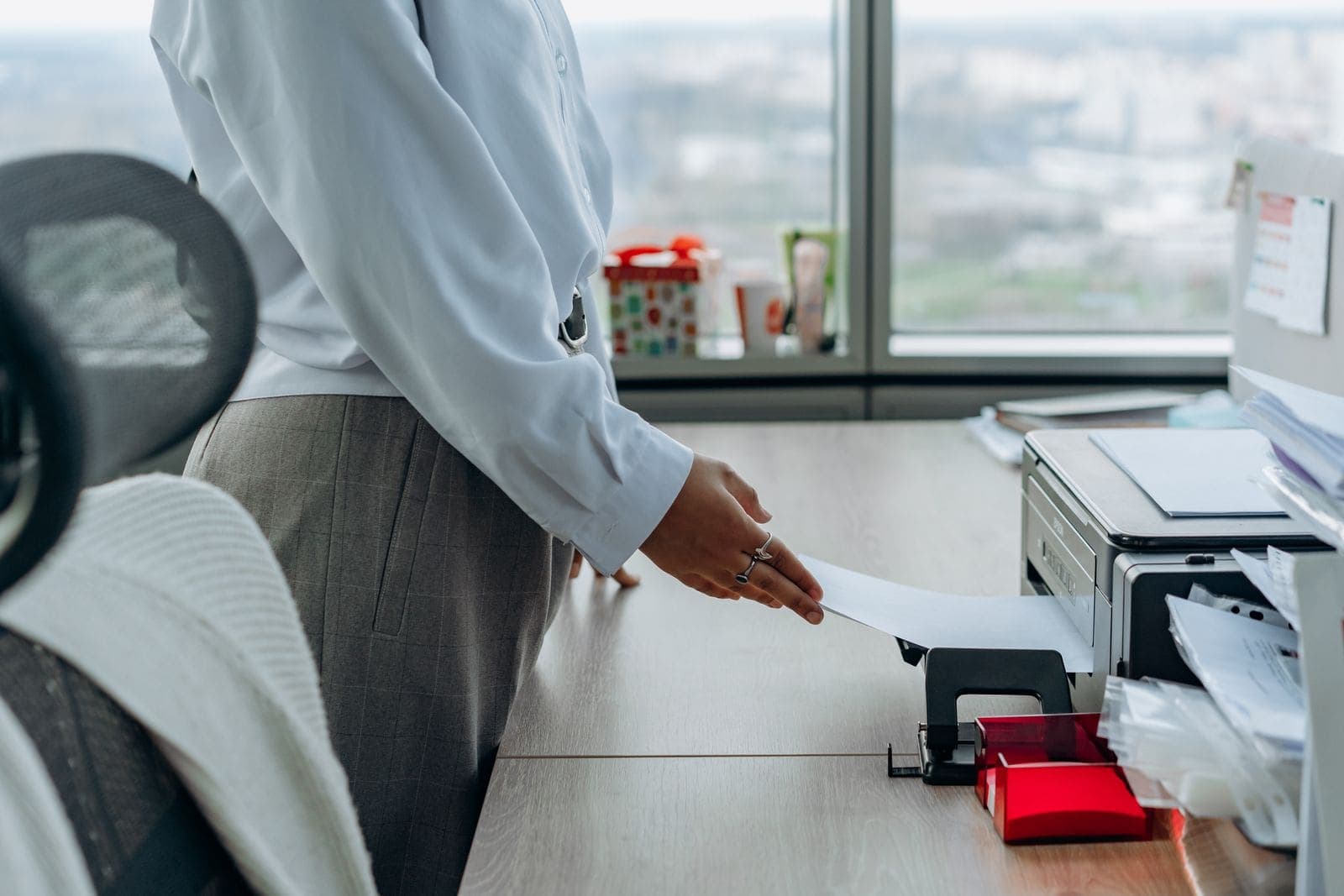 Woman in a white shirt feeding a sheet of paper into a multifunction printer on a desk