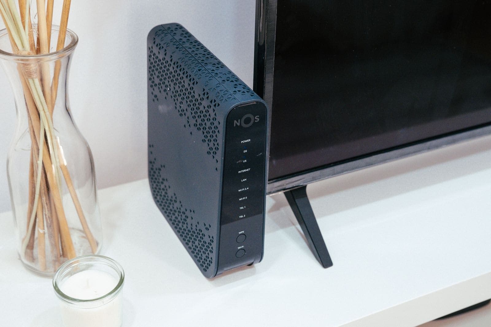 Black internet router placed near a television, with Internet, LAN, Wi-Fi and TEL 1 and TEL 2 indicator lights