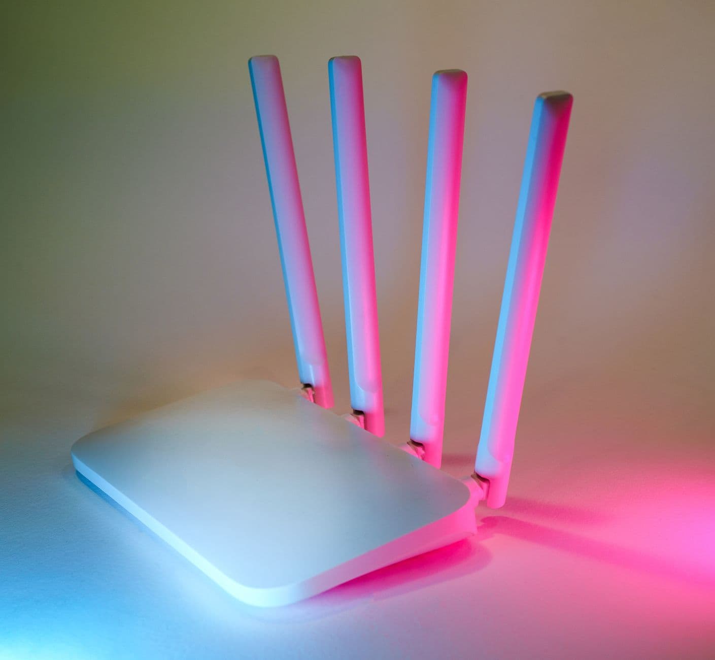 Box routeur Wi-Fi blanc à quatre antennes, posé sur une surface claire éclairée de rose et de bleu