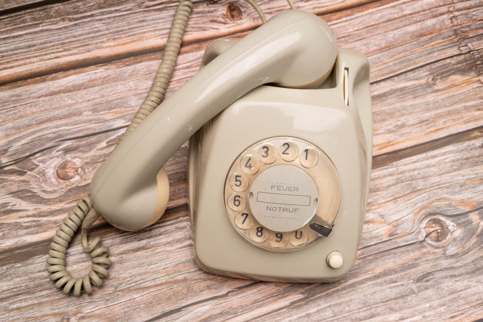 Ancien téléphone fixe à cadran rotatif beige, combiné décroché, posé sur des planches de bois usées