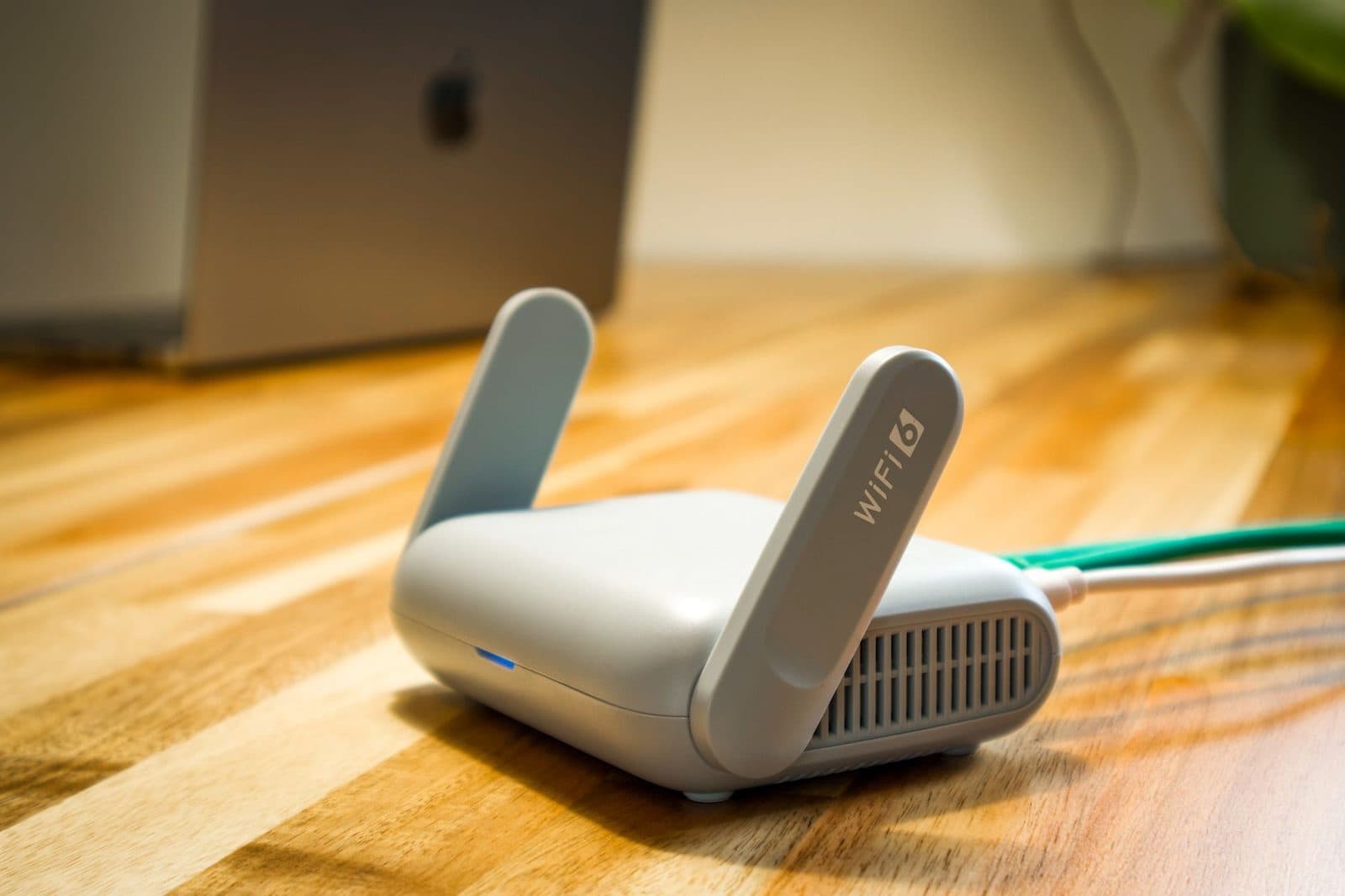 Routeur Wi-Fi 6 blanc avec antennes relevées et câble Ethernet vert, posé sur un parquet