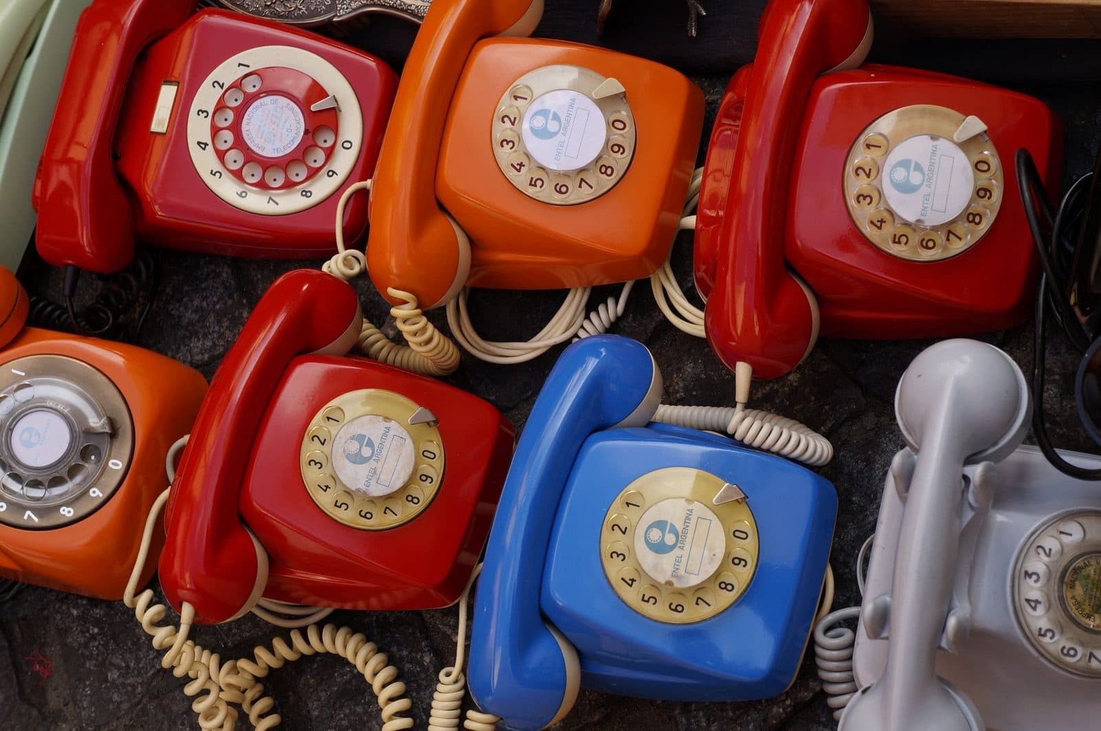 Vintage-Wählscheibentelefone in verschiedenen Farben, nebeneinander aufgestellt mit ihren Kabeln