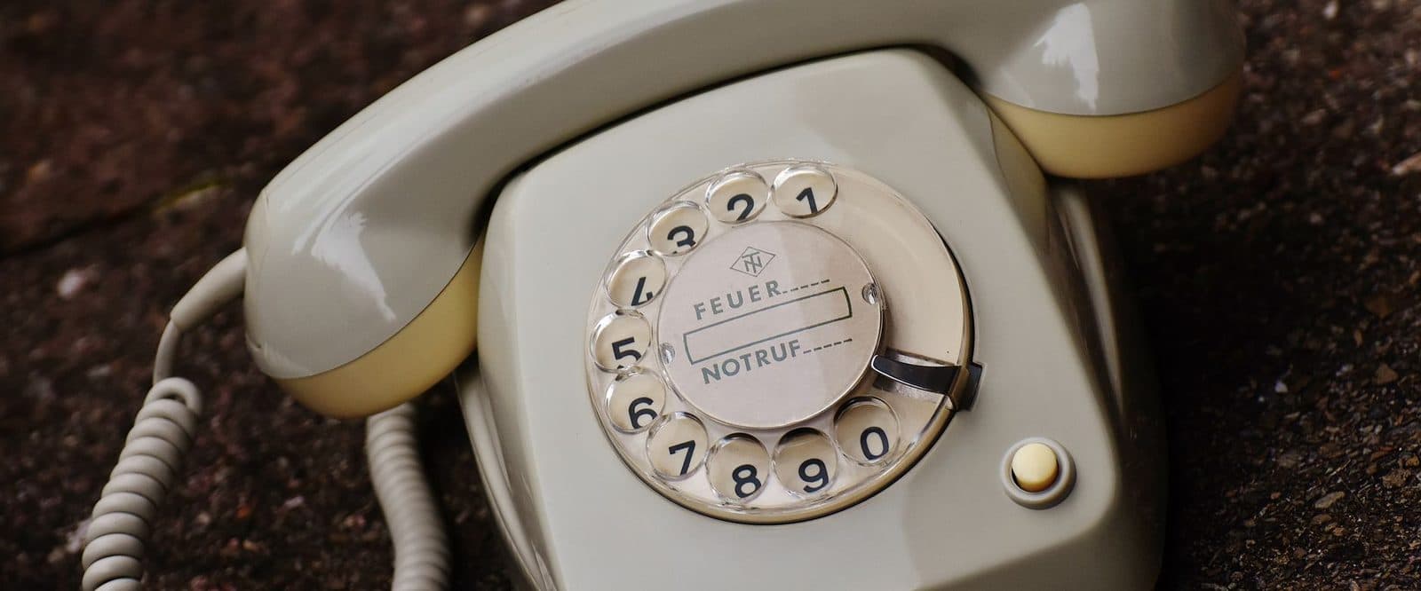 Altes beigefarbenes Wählscheibentelefon mit Hörer und Spiralkabel auf einem Kiesboden