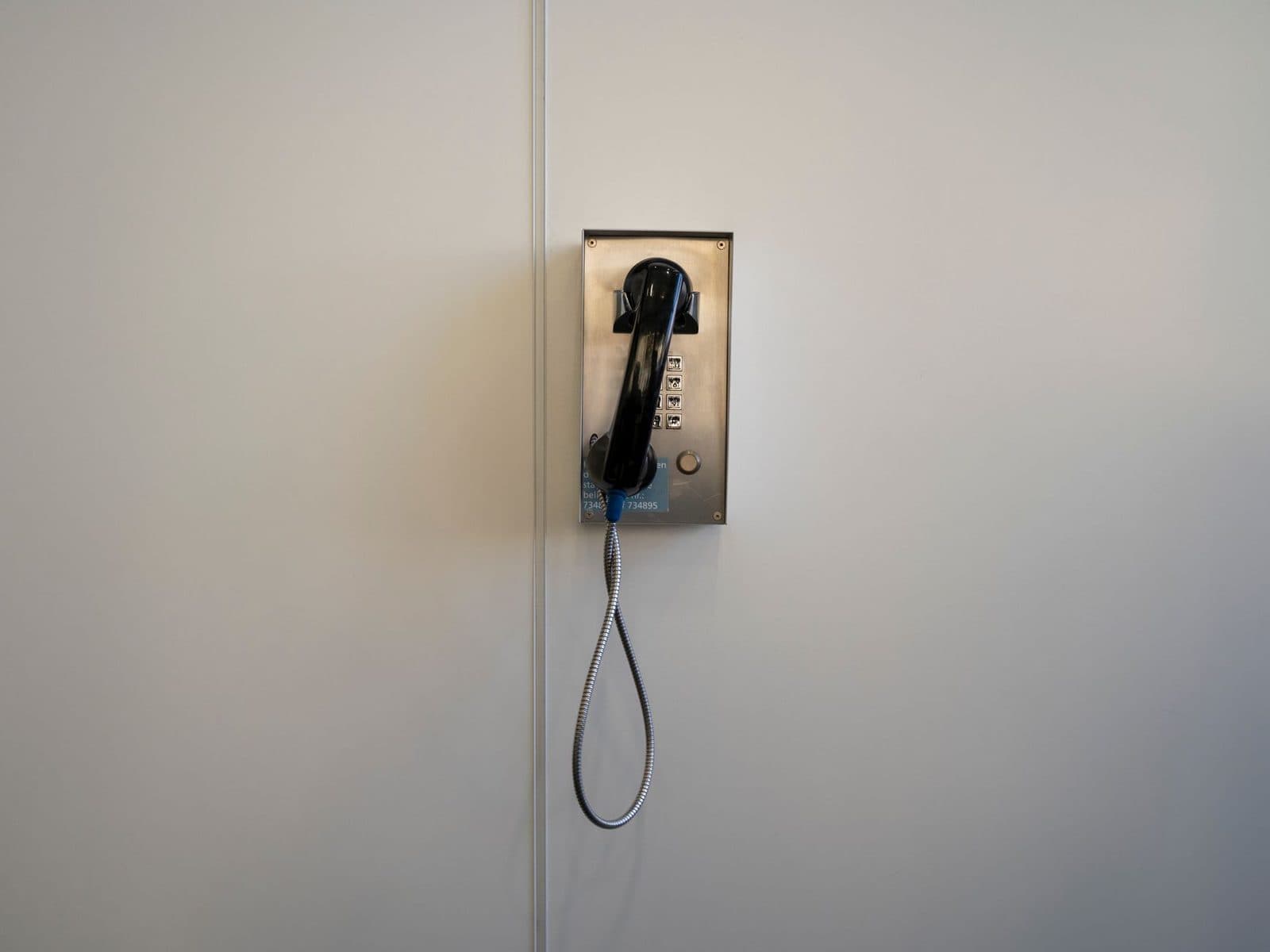 Schwarzes schnurgebundenes Wandtelefon mit Hörer und Metalltastatur, montiert an einer weißen Wand