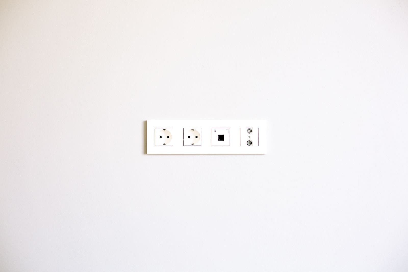 Placca da muro bianca con due prese elettriche, una presa RJ45 e prese TV su una parete chiara
